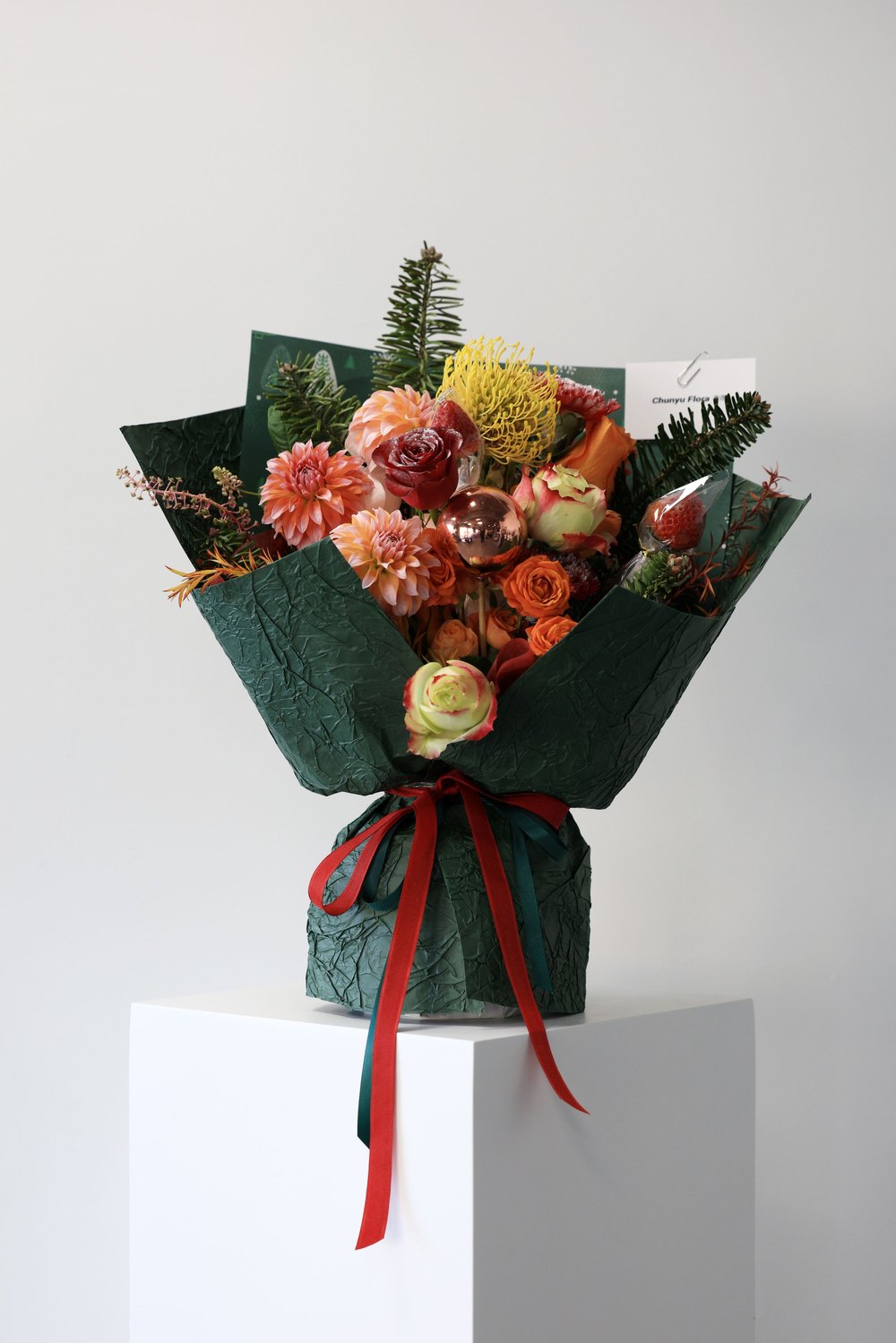 A finished bouquet of terracotta dahlias and roses wrapped in deep green paper with a red ribbon.